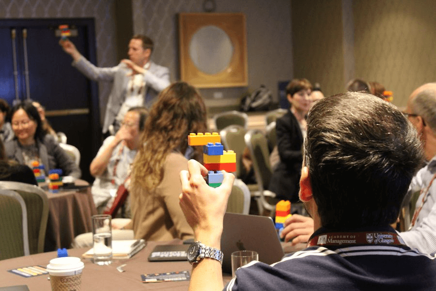 A person learning the i5 Framework from a presenter in a conference room while building legos
